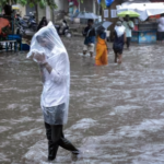 A man covers himself with a plastic sheet amid heavy rainfall in Surat.