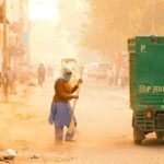 Municipal workers sweeping a dusty urban road in India, highlighting road dust pollution and air quality challenges.
