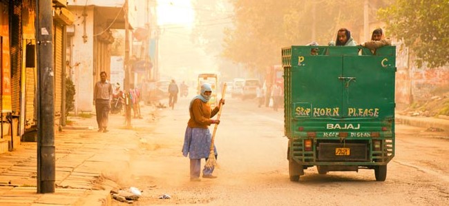 Municipal workers sweeping a dusty urban road in India, highlighting road dust pollution and air quality challenges.